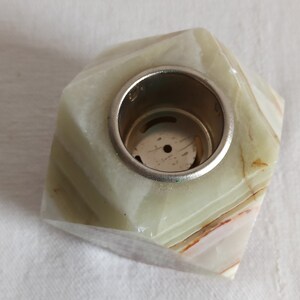 Puede incluir: Un portavelas de m&aacute;rmol verde y blanco con un inserto de metal plateado. El portavelas tiene una forma geom&eacute;trica con m&uacute;ltiples facetas.