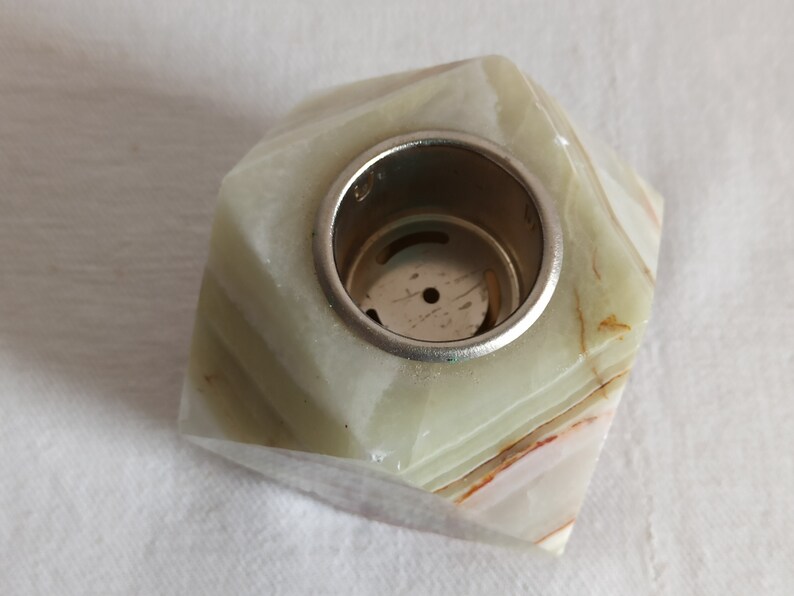 Puede incluir: Un portavelas de m&aacute;rmol verde y blanco con un inserto de metal plateado. El portavelas tiene una forma geom&eacute;trica con m&uacute;ltiples facetas.