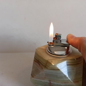 Puede incluir: Un encendedor de mesa de m&aacute;rmol verde y blanco con un encendedor plateado en la parte superior. El encendedor est&aacute; encendido y la llama es visible.