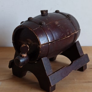 May include: A dark brown wooden barrel with a small wooden tap, sitting on a wooden stand. The barrel has a worn, rustic look.