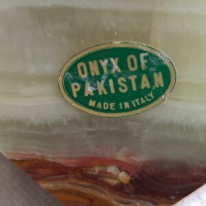 Puede incluir: Una pegatina ovalada verde con el texto "ONYX OF PAKISTAN MADE IN ITALY" sobre una superficie de m&aacute;rmol verde claro y marr&oacute;n.