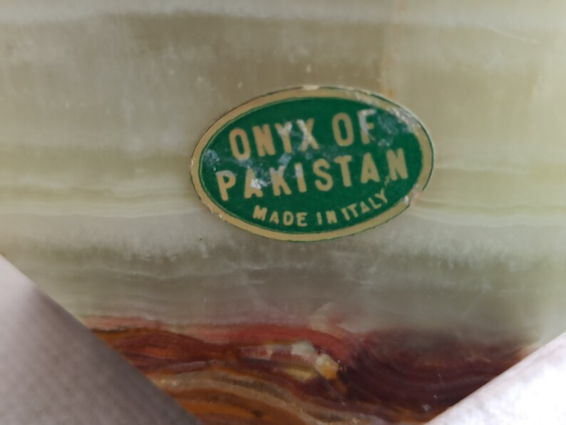 Puede incluir: Una pegatina ovalada verde con el texto "ONYX OF PAKISTAN MADE IN ITALY" sobre una superficie de m&aacute;rmol verde claro y marr&oacute;n.