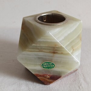 Puede incluir: Un portavelas de &oacute;nix verde y blanco con una parte superior plateada. El portavelas tiene forma de pir&aacute;mide y lleva una etiqueta que dice "Onyx of Pakistan Made in Italy".