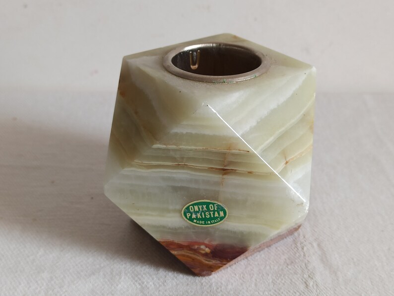 Puede incluir: Un portavelas de &oacute;nix verde y blanco con una parte superior plateada. El portavelas tiene forma de pir&aacute;mide y lleva una etiqueta que dice "Onyx of Pakistan Made in Italy".