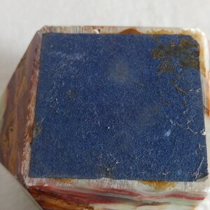 Puede incluir: Una peque&ntilde;a caja rectangular multicolor con un forro de fieltro azul. La caja est&aacute; hecha de un material de piedra en capas.