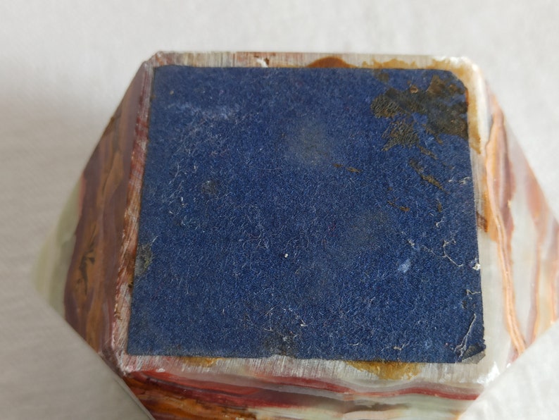 Puede incluir: Una peque&ntilde;a caja rectangular multicolor con un forro de fieltro azul. La caja est&aacute; hecha de un material de piedra en capas.