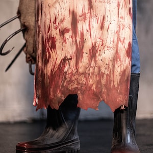 May include: A pair of black rubber boots with red splatters on them. The boots are worn and have a distressed look. The boots are standing on a concrete floor.