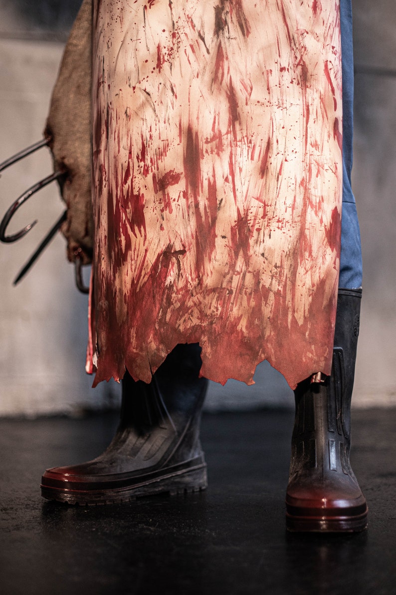 May include: A pair of black rubber boots with red splatters on them. The boots are worn and have a distressed look. The boots are standing on a concrete floor.