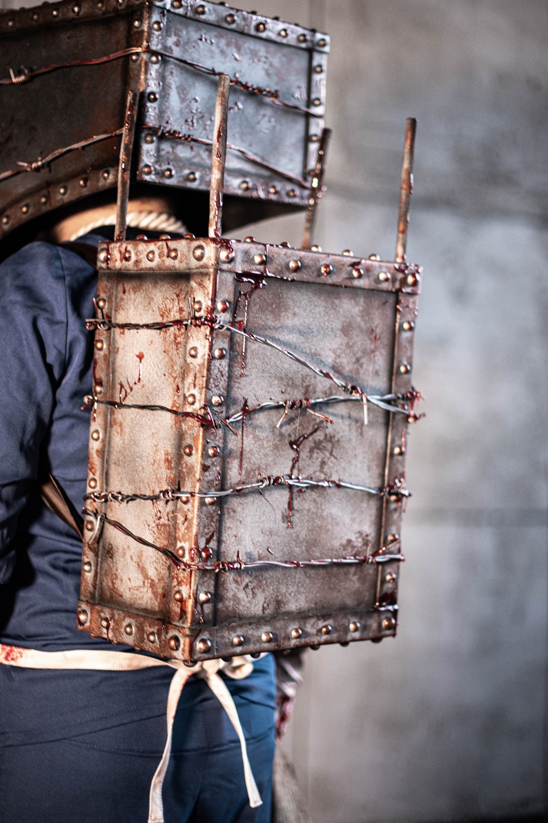 May include: A person wearing a costume with a rusty metal box on their back. The box is covered in barbed wire and has blood splatters on it.