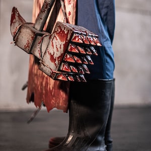 May include: A bloody, spiked hammer with a metal handle is held by a person wearing blue trousers and black boots.