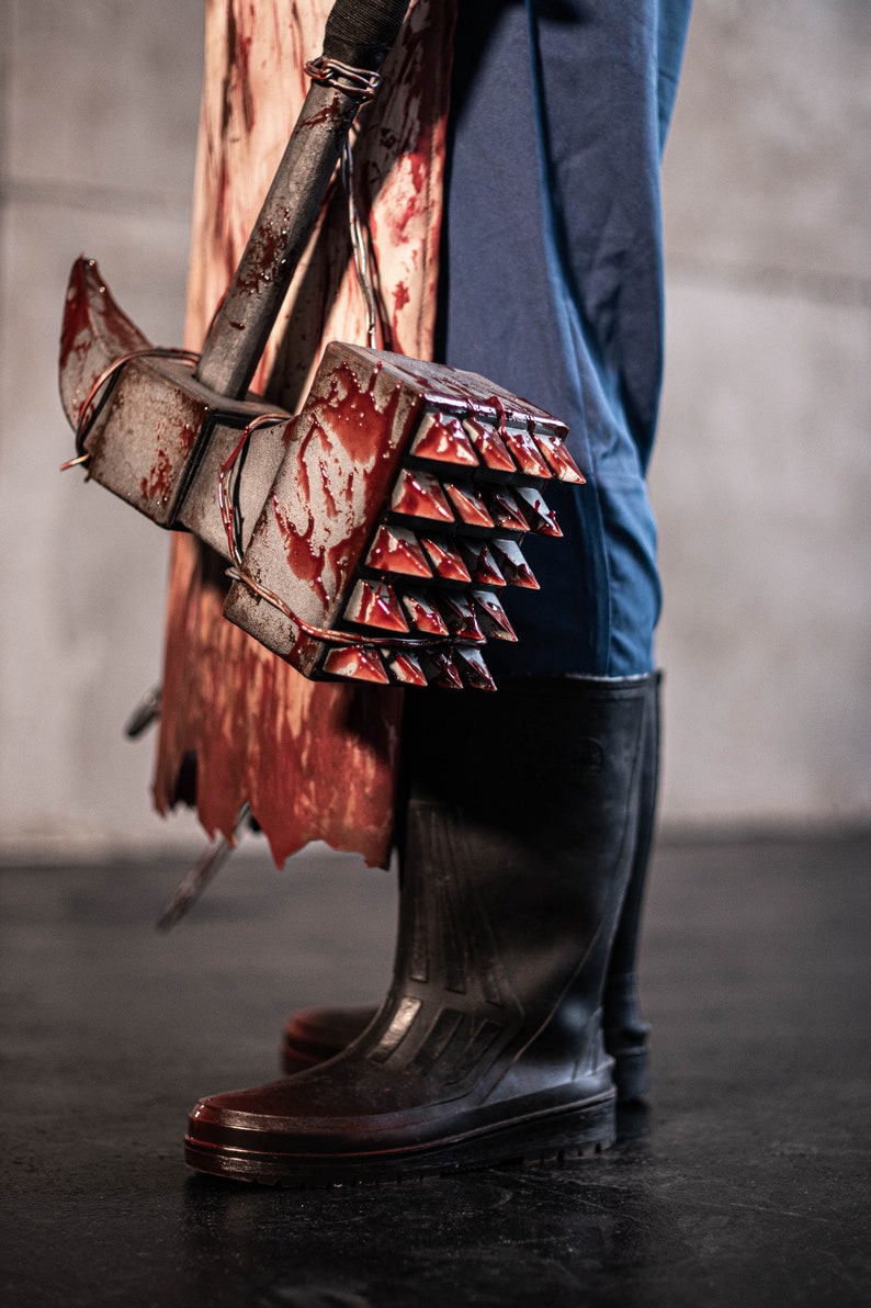 May include: A bloody, spiked hammer with a metal handle is held by a person wearing blue trousers and black boots.