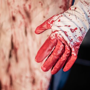 May include: A white glove with red blood splatters on it. The glove is partially covering a bloody surface.