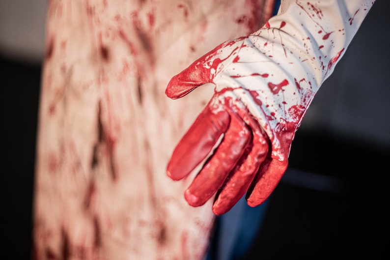 May include: A white glove with red blood splatters on it. The glove is partially covering a bloody surface.