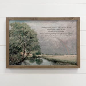 May include: A framed landscape print featuring a serene river scene with a tree and a rainbow. The artwork has a muted color palette with text from Genesis 9:13-16. The frame is a natural wood color.