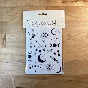 Könnte beinhalten: Ein Blatt mit temporären Tattoos mit einem himmlischen Thema. Das Blatt zeigt verschiedene Designs in Schwarz und Weiß, darunter Monde, Sterne und ein Auge mit Strahlen. Der Text "celestial temporary tattoos" ist auf dem Blatt gedruckt.