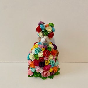 May include: A white mouse figurine wearing a crown of colorful paper flowers. The mouse is surrounded by a large bouquet of colorful paper flowers.