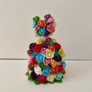 May include: A colorful paper flower figurine with a dress made of many small flowers in various colors, including pink, blue, yellow, orange, and green.