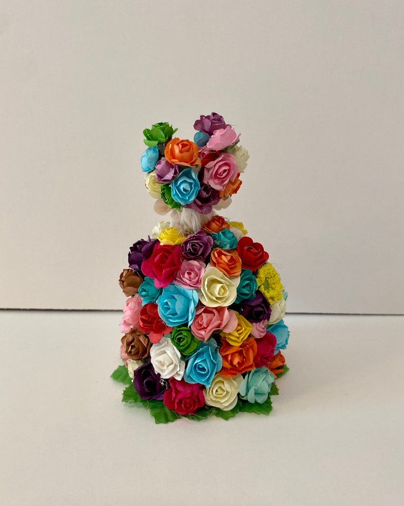 May include: A colorful paper flower figurine with a dress made of many small flowers in various colors, including pink, blue, yellow, orange, and green.