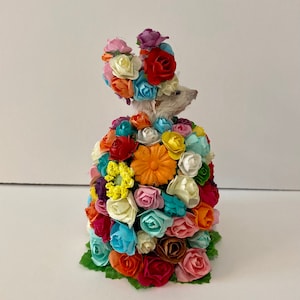 May include: A small white mouse wearing a crown and dress made entirely of colorful paper flowers.
