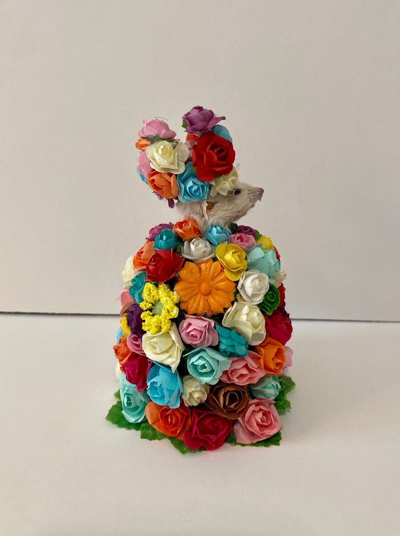 May include: A small white mouse wearing a crown and dress made entirely of colorful paper flowers.