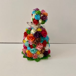 May include: A small white mouse wearing a crown of colorful paper flowers. The mouse is surrounded by a large bouquet of colorful paper flowers.