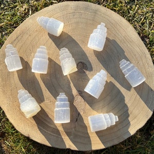 May include: A collection of ten selenite crystal towers, each with a unique shape and size, arranged on a wooden surface. The crystals are white and translucent, with a smooth, polished finish.