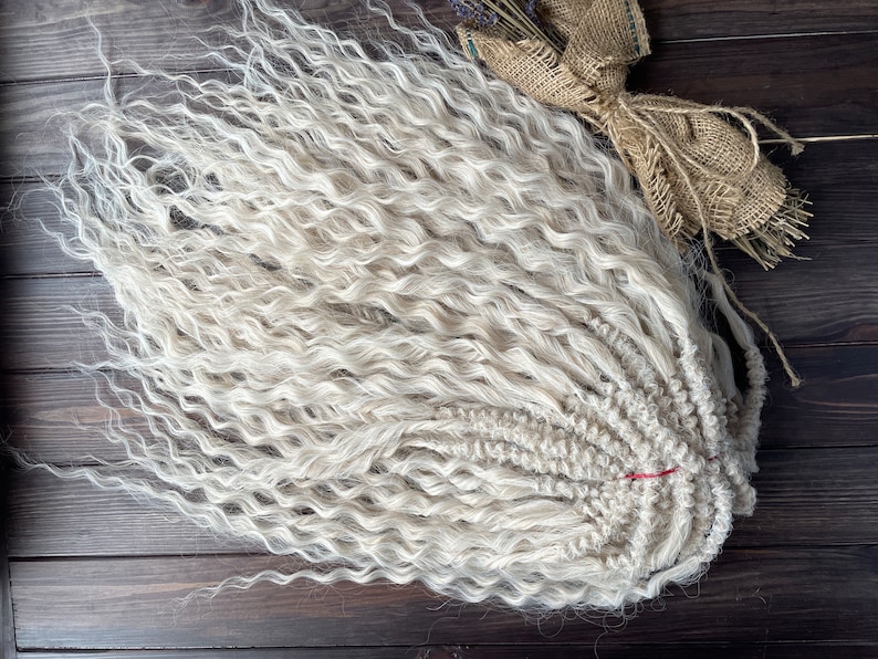 May include: A bundle of long, white, curly synthetic hair extensions. The hair is arranged in a loose braid and is ready to be used for braiding or weaving.