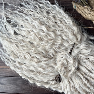 May include: A bundle of white curly hair extensions. The hair is arranged in a loose braid and secured with a metal pin.