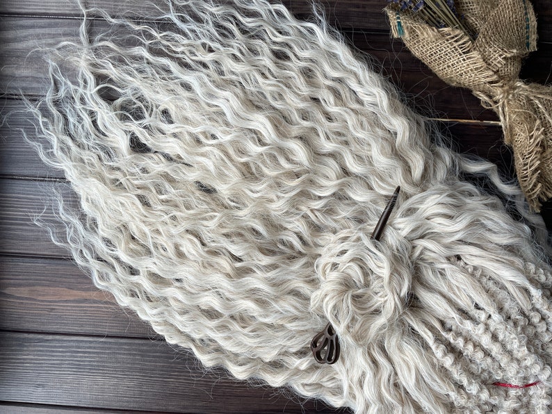 May include: A bundle of white curly hair extensions. The hair is arranged in a loose braid and secured with a metal pin.