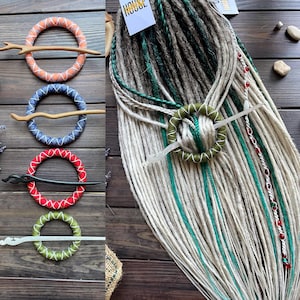 Op de afbeelding: Een assortiment haaraccessoires, waaronder kleurrijke dreadlock kralen en haar wraps. De wraps zijn oranje, blauw, rood en groen, elk met een bijpassende stok. De dreadlocks zijn wit, groen en bruin.