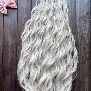 May include: A long, wavy, platinum blonde hair extension. The hair is thick and full, with a natural-looking wave.