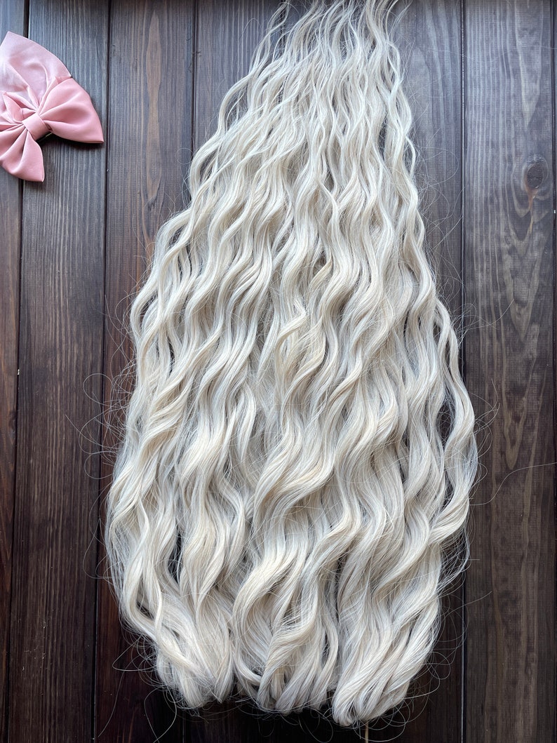 May include: A long, wavy, platinum blonde hair extension. The hair is thick and full, with a natural-looking wave.