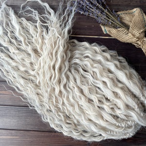 May include: A bundle of white curly hair extensions. The hair is arranged in a loose, wavy pile.