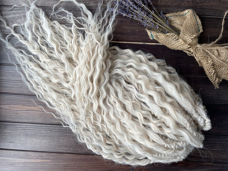 May include: A bundle of white curly hair extensions. The hair is arranged in a loose, wavy pile.
