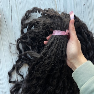 May include: A bundle of long, dark brown curly hair extensions tied with a pink ribbon.