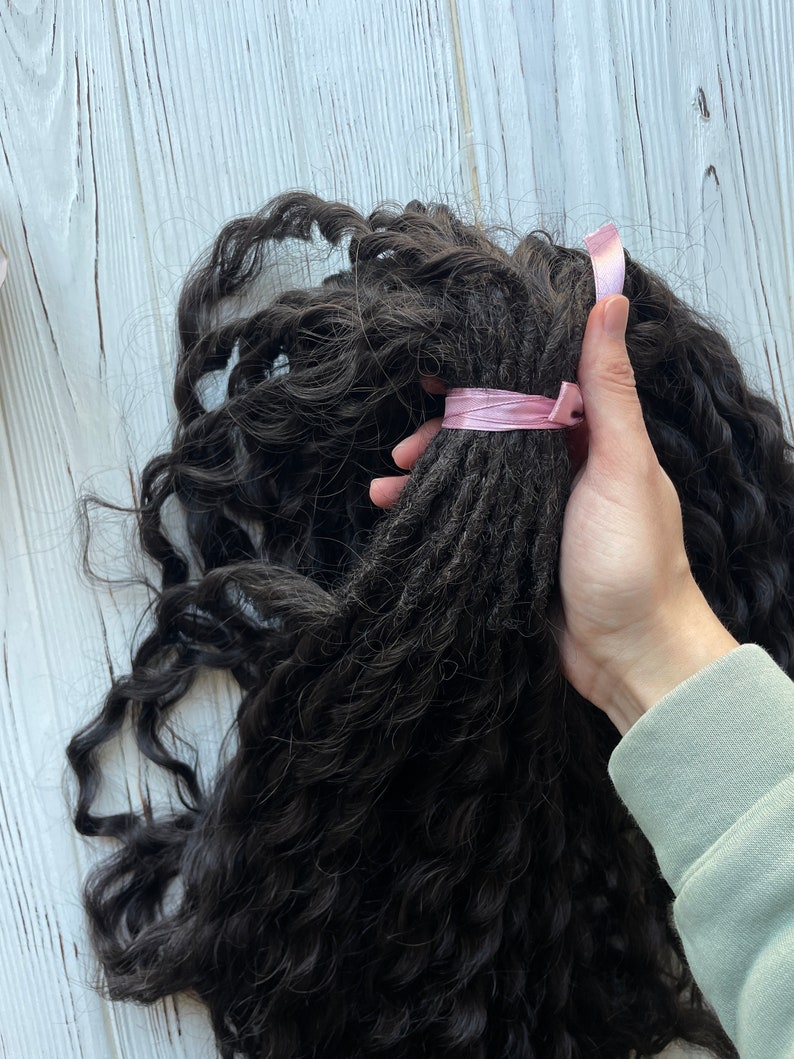 May include: A bundle of long, dark brown curly hair extensions tied with a pink ribbon.