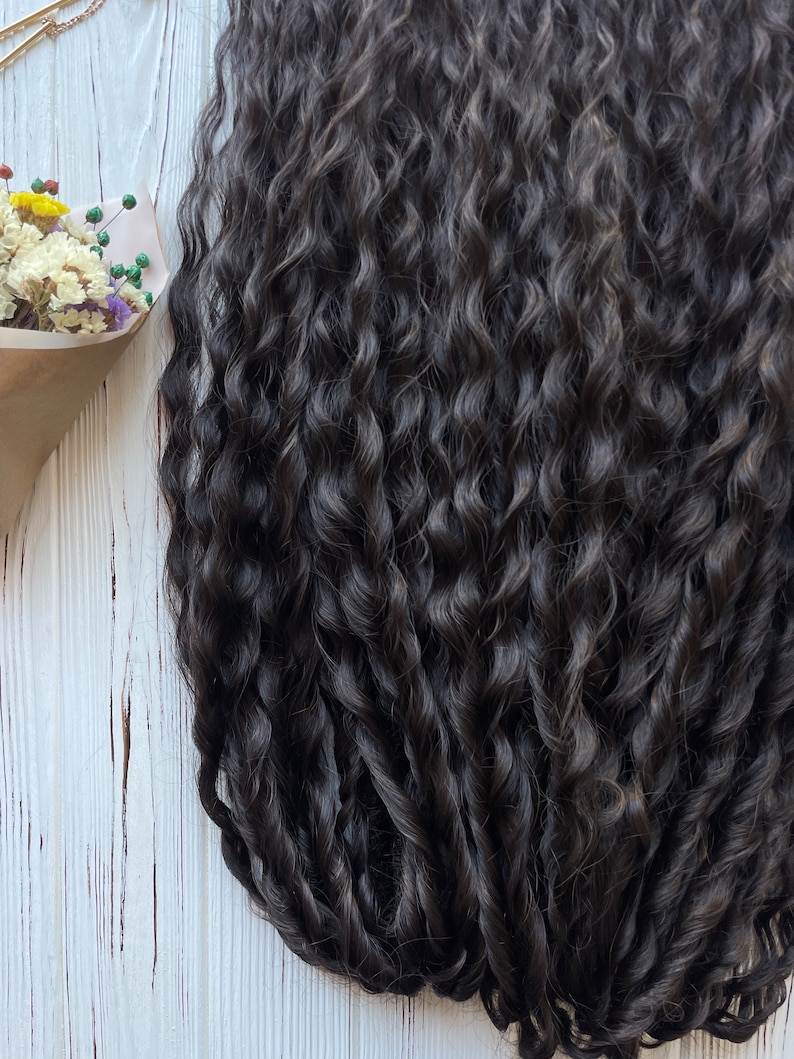 May include: A close-up of a bundle of dark brown curly hair extensions. The hair is arranged in a loose, flowing style, showcasing its natural texture and volume.
