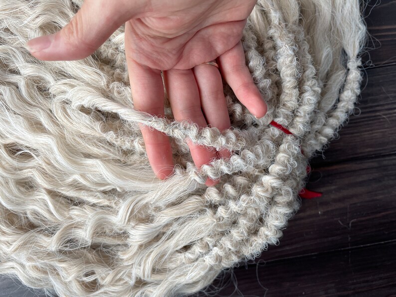 May include: A close-up of a bundle of white, curly, synthetic hair extensions. The hair is arranged in a loose braid and is soft and fluffy.