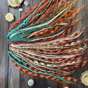 May include: A set of synthetic hair extensions in shades of brown, blonde, and teal. The extensions are braided and arranged in a fan shape on a wooden surface.