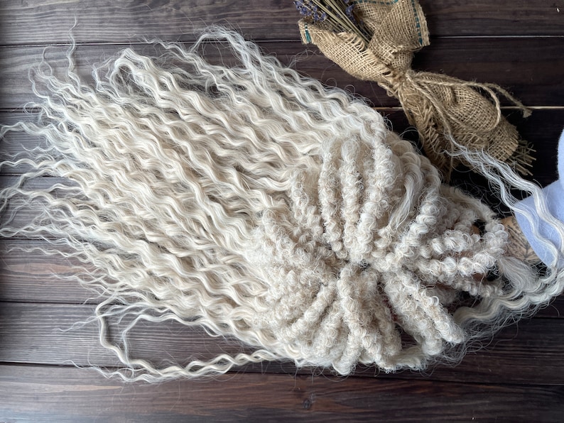 May include: A bundle of long, white, curly hair extensions. The hair is arranged in a loose, circular shape.