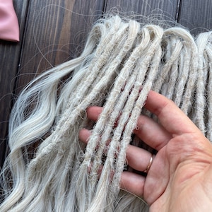 May include: A bundle of light blonde synthetic dreadlocks. The dreadlocks are made of a soft, textured material and are approximately 24 inches long.