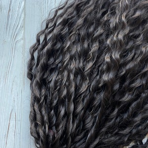 May include: A close-up of a bundle of dark brown curly human hair extensions. The hair is arranged in a loose, wavy pattern, showing the texture and thickness of the strands.