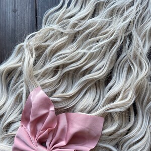 May include: A long, wavy, light blonde hair extension with a large, dusty rose colored bow.