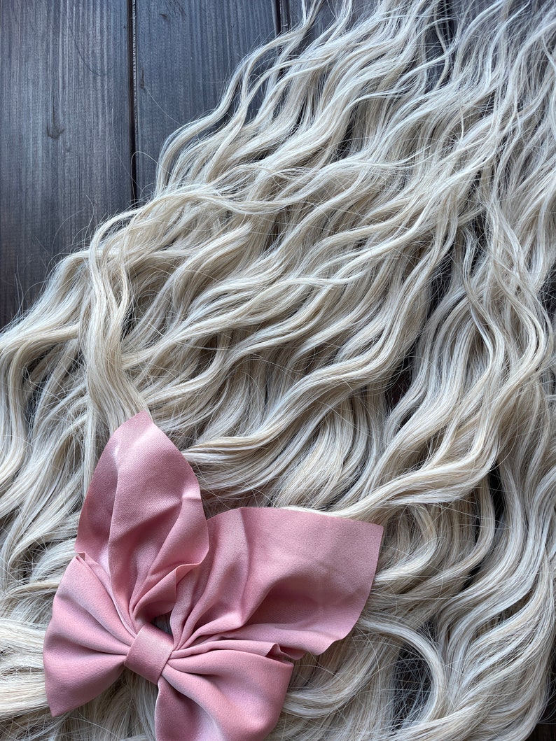 May include: A long, wavy, light blonde hair extension with a large, dusty rose colored bow.