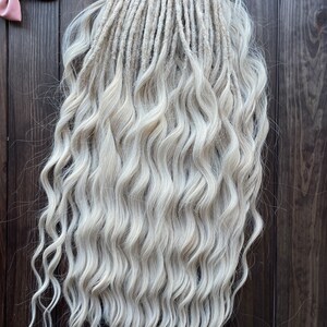 May include: A set of long, wavy, white synthetic dreadlocks. The dreadlocks are arranged in a straight line and are hanging down.