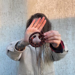 May include: A person is holding a coiled rope made of black and orange yarn. The rope is about 25 cm in diameter and is coiled into a circle.