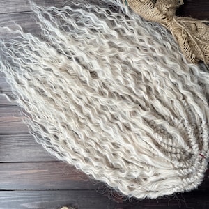 May include: A bundle of long, white, wavy synthetic hair extensions. The hair is arranged in a loose braid.