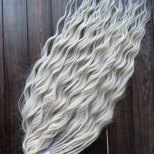May include: A bundle of long, wavy, white synthetic dreadlocks. The dreadlocks are tied together with a purple ribbon.