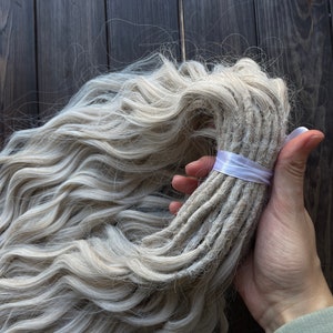 May include: A bundle of long, wavy, light blonde synthetic dreadlocks tied with a white ribbon.