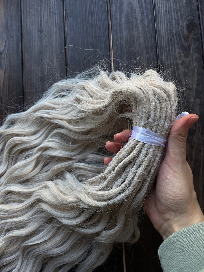 May include: A bundle of long, wavy, light blonde synthetic dreadlocks tied with a white ribbon.